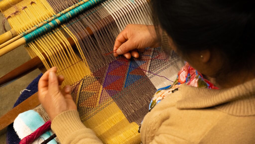 A woman is weaving on a loom.